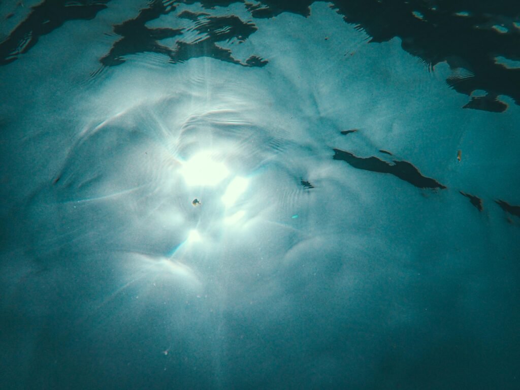 Ethereal sunlight piercing through the calm water creating a dreamy ripple effect.